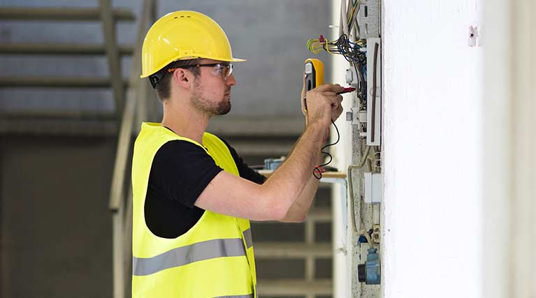 Apprentice electrician fixes wiring on a housing unit.